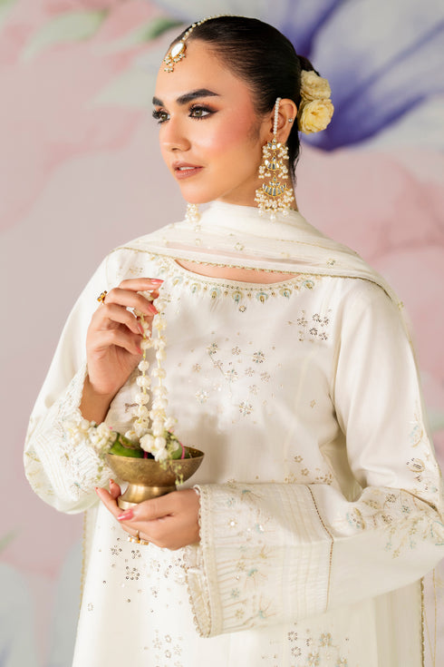 Woman in traditional white outfit with jewelry against a soft pink and purple background