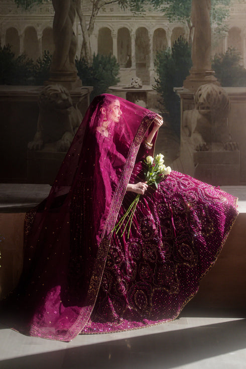 Woman in a purple embroidered dress holding flowers in an outdoor setting with columns and statues.