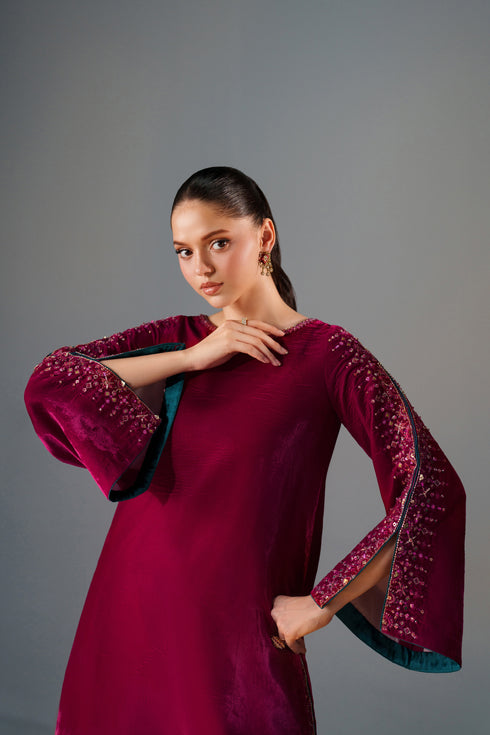 Woman wearing a burgundy dress with intricate detailing on a gray background