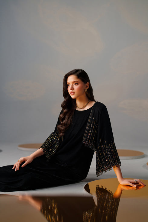 Woman in a black dress with embellishments sitting on a reflective surface.