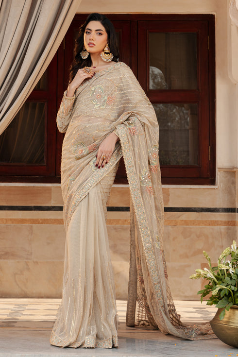 NAQSHI Ramish skin‑hued net saree draped front view showing boat‑neck raw‑silk blouse, fitted sleeves and heavy hand embellishments of kora, sitara & floral motifs