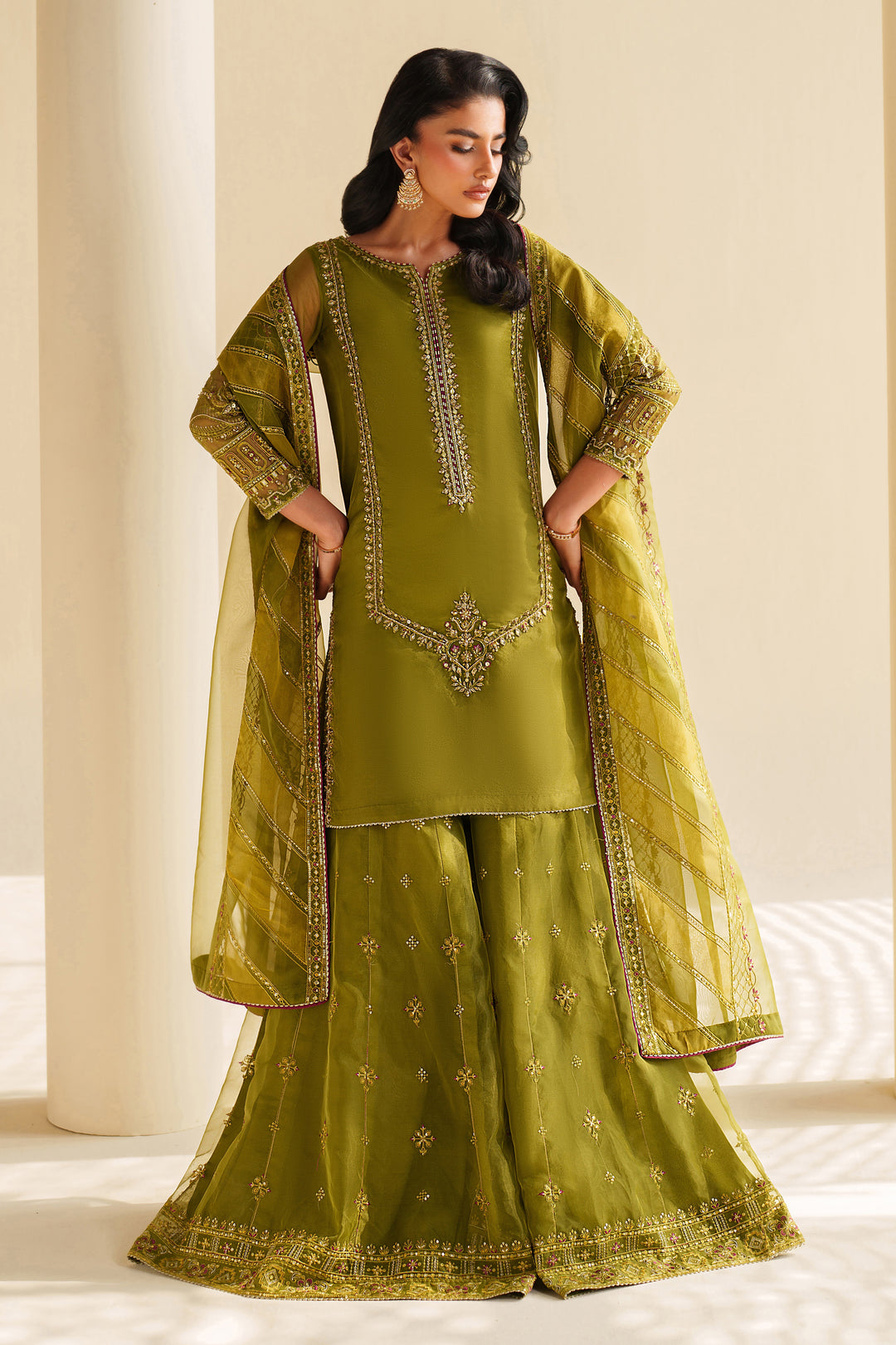 Woman wearing a green traditional outfit with embroidery against a neutral background