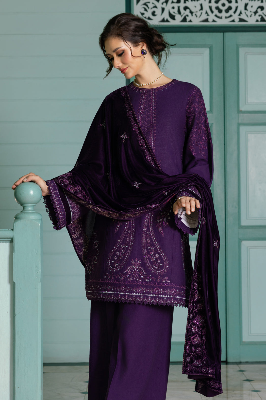 Woman wearing a purple embroidered outfit against a light green wall.