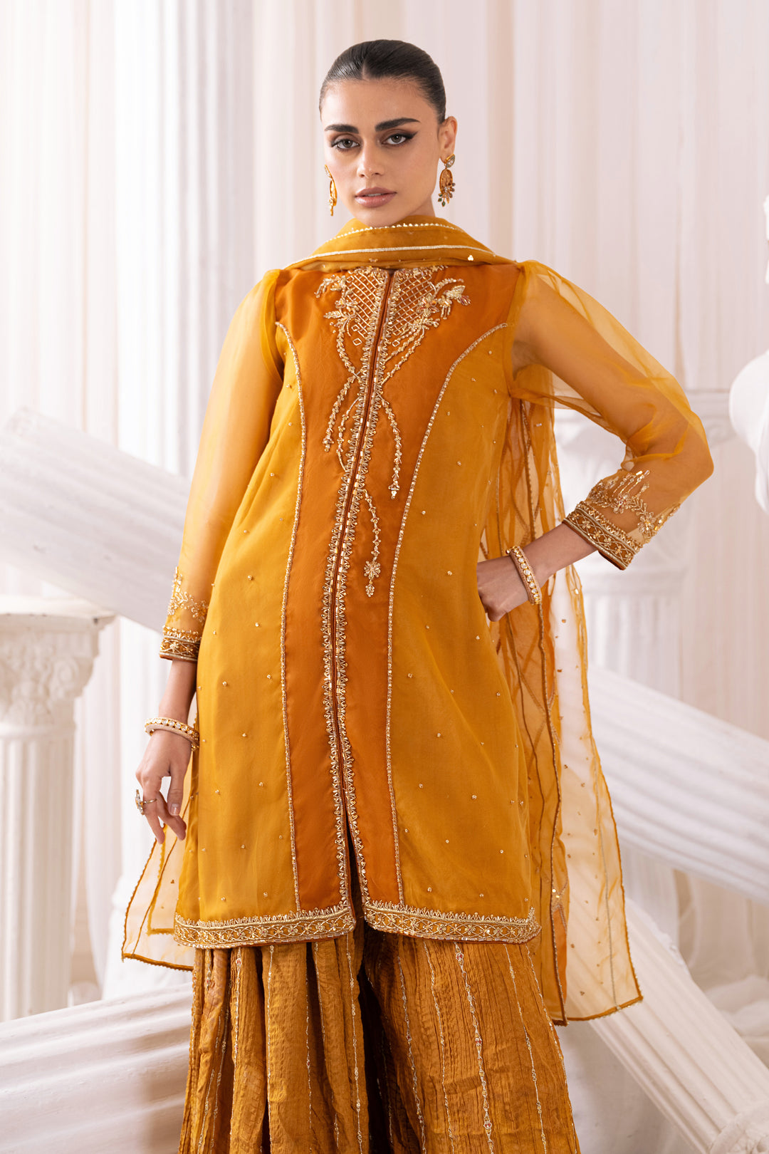 Side view showing Naqshi Sumbul A‑line cutline, jeweled adda‑border sleeves and flowing crushed sharara beneath ornate organza dupatta.