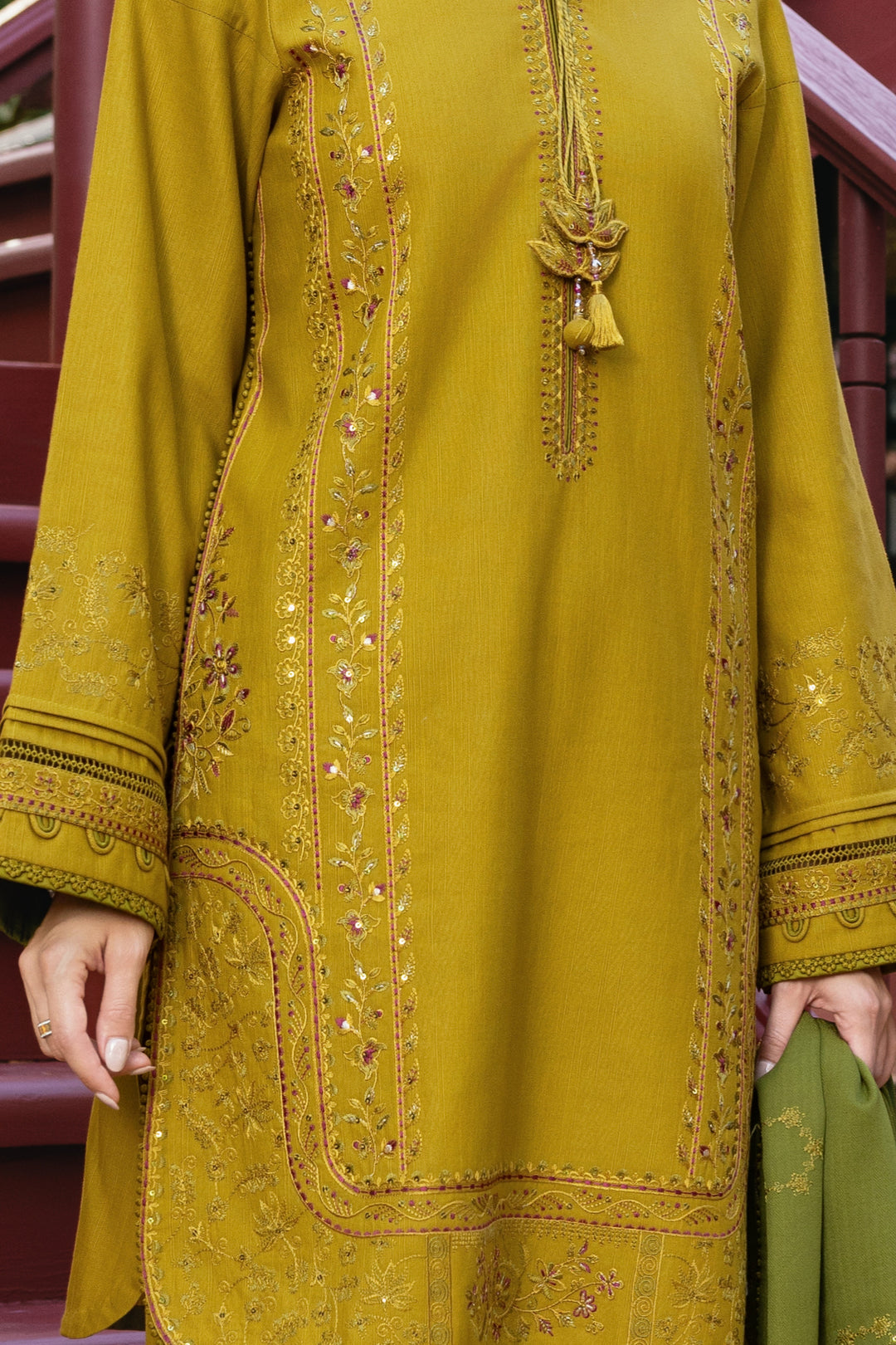 Mustard yellow embroidered traditional outfit with green pants, held by a hand.