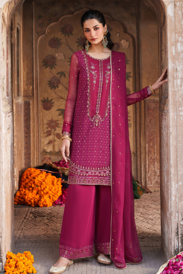 Woman in a traditional pink embroidered outfit standing in an ornate doorway.