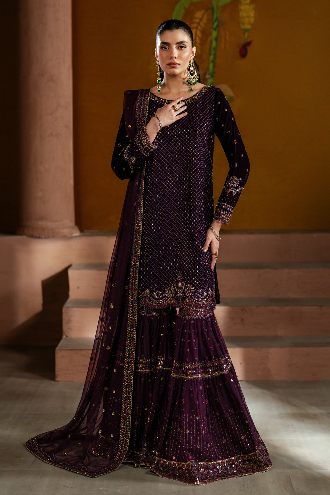 Woman in a traditional dark purple embroidered outfit standing on steps with a warm-toned background