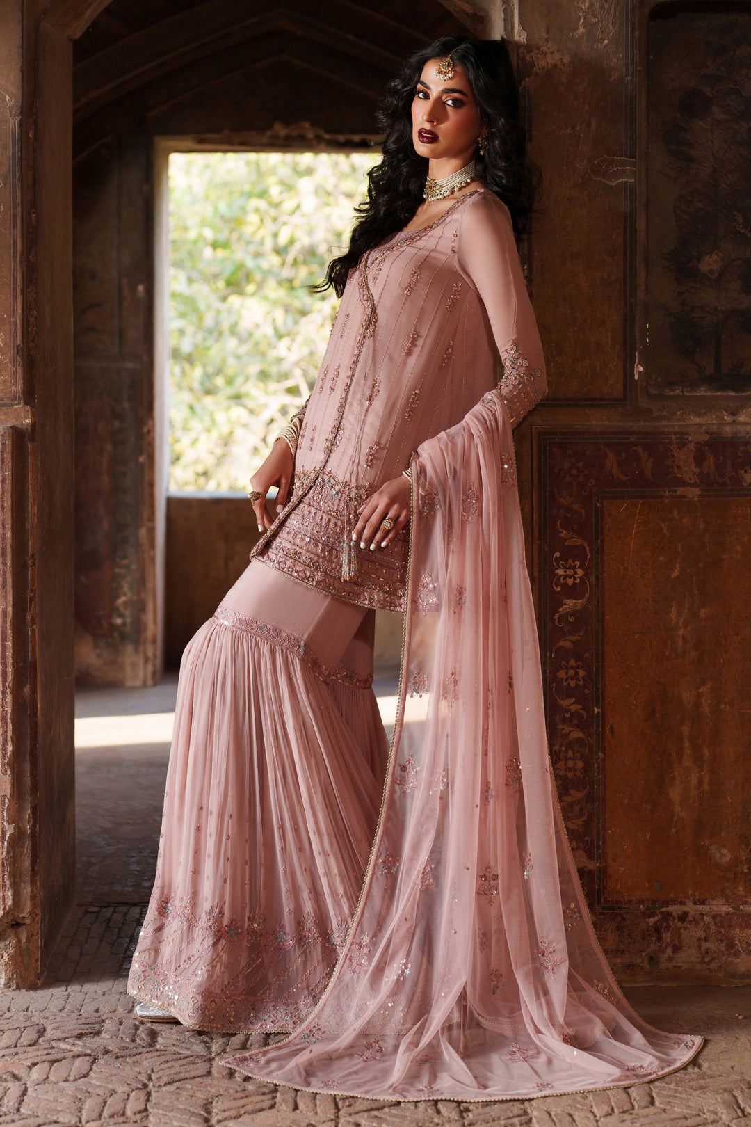Woman in a pink traditional outfit standing in an ornate doorway.