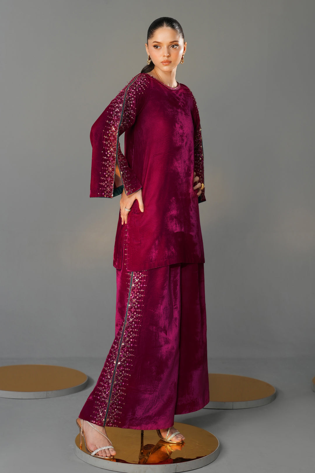 Woman wearing a burgundy traditional outfit with intricate designs on a gray background
