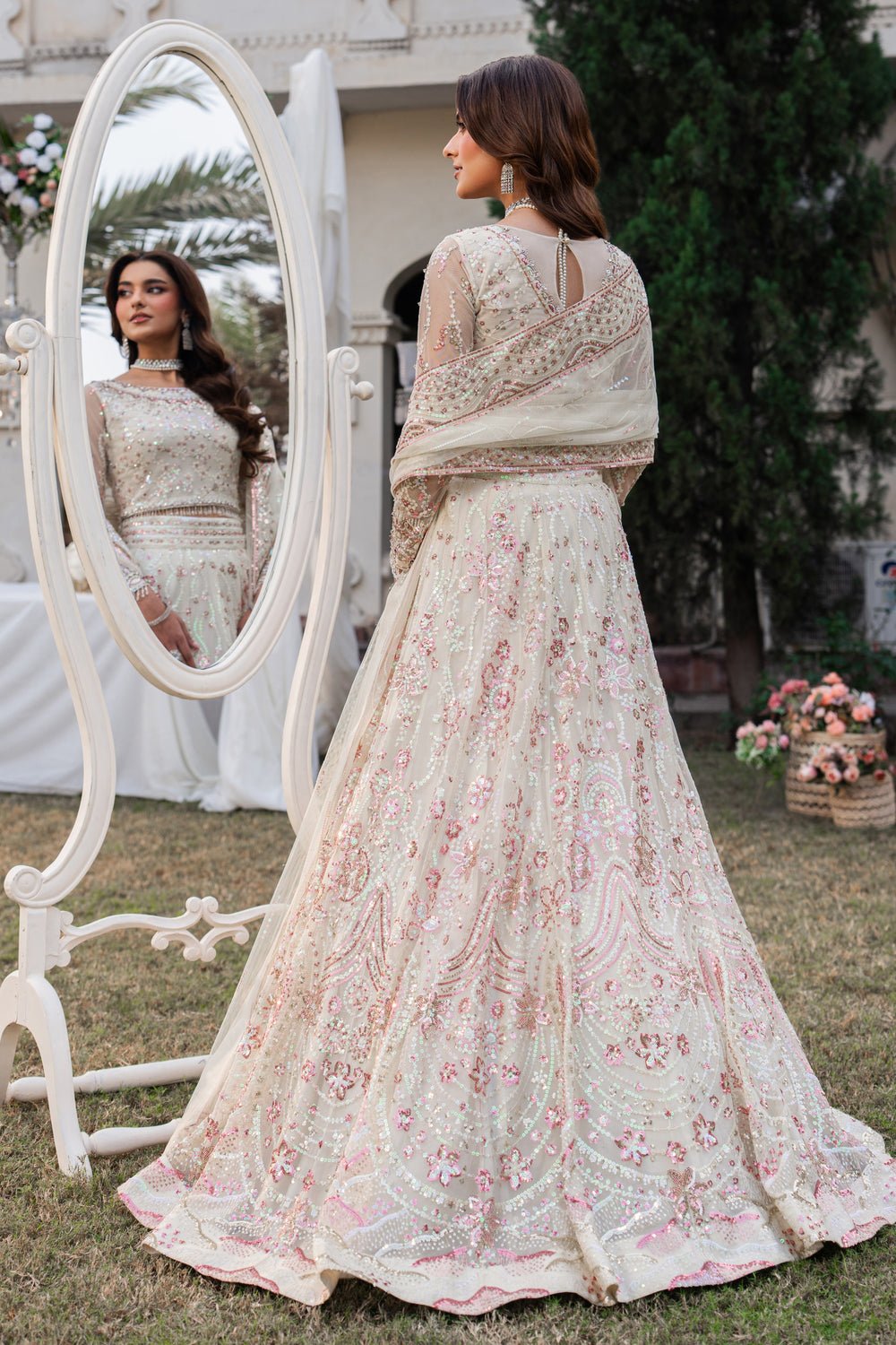 Woman in a floral embroidered outfit standing next to a mirror outdoors.