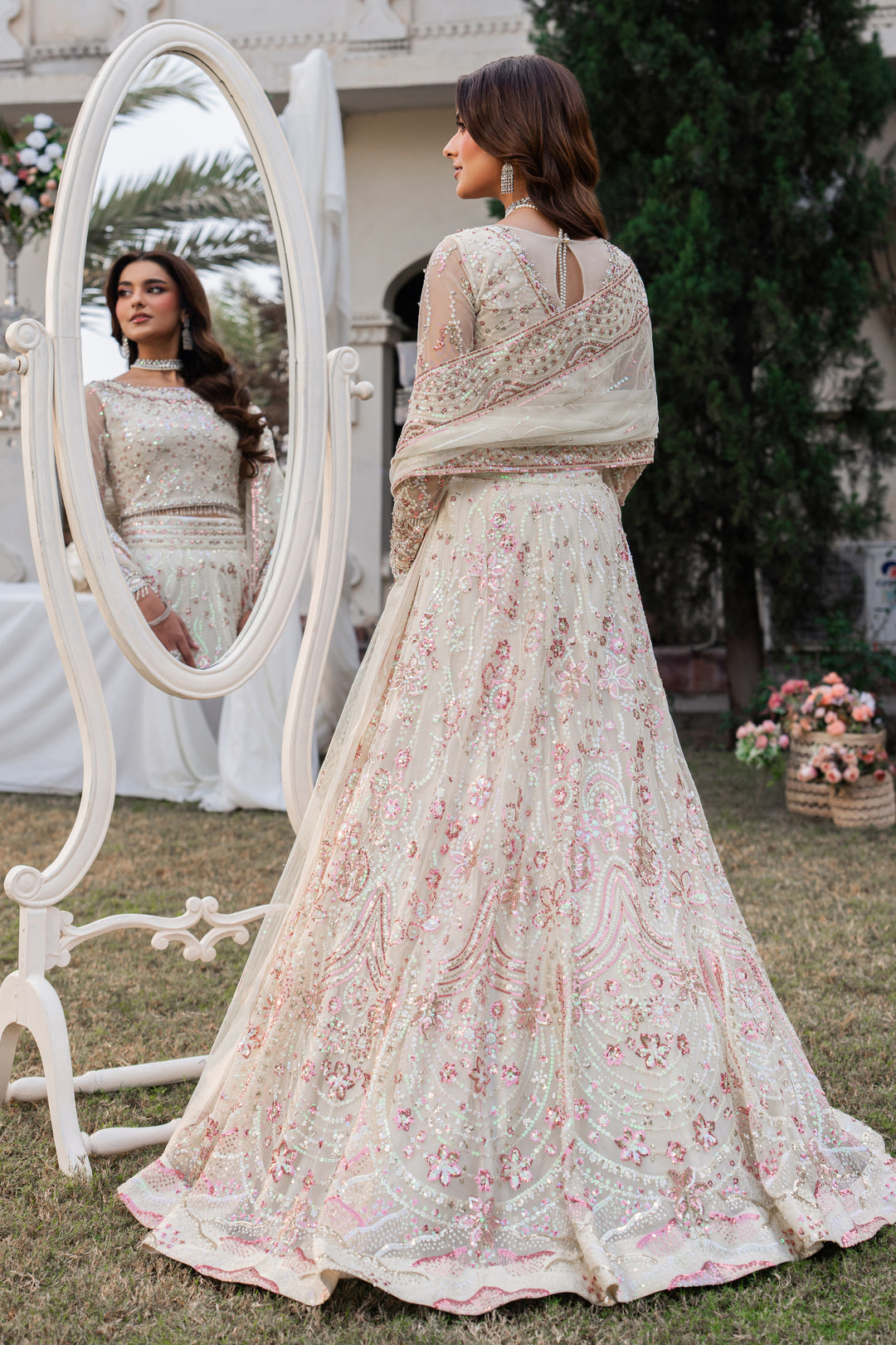 Woman in a floral embroidered outfit standing next to a mirror outdoors.