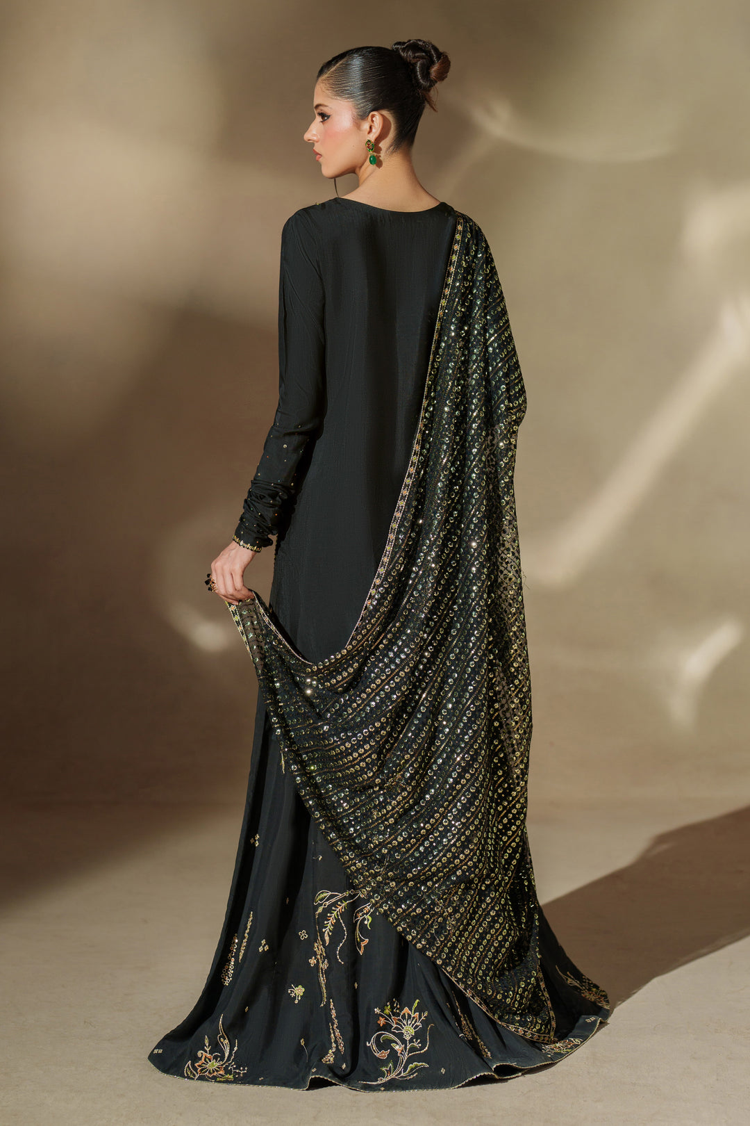 Side view of NAQSHI Misam black raw silk sharara set showing embroidered V-neck shirt, flowing sharara and matching net dupatta for festive events