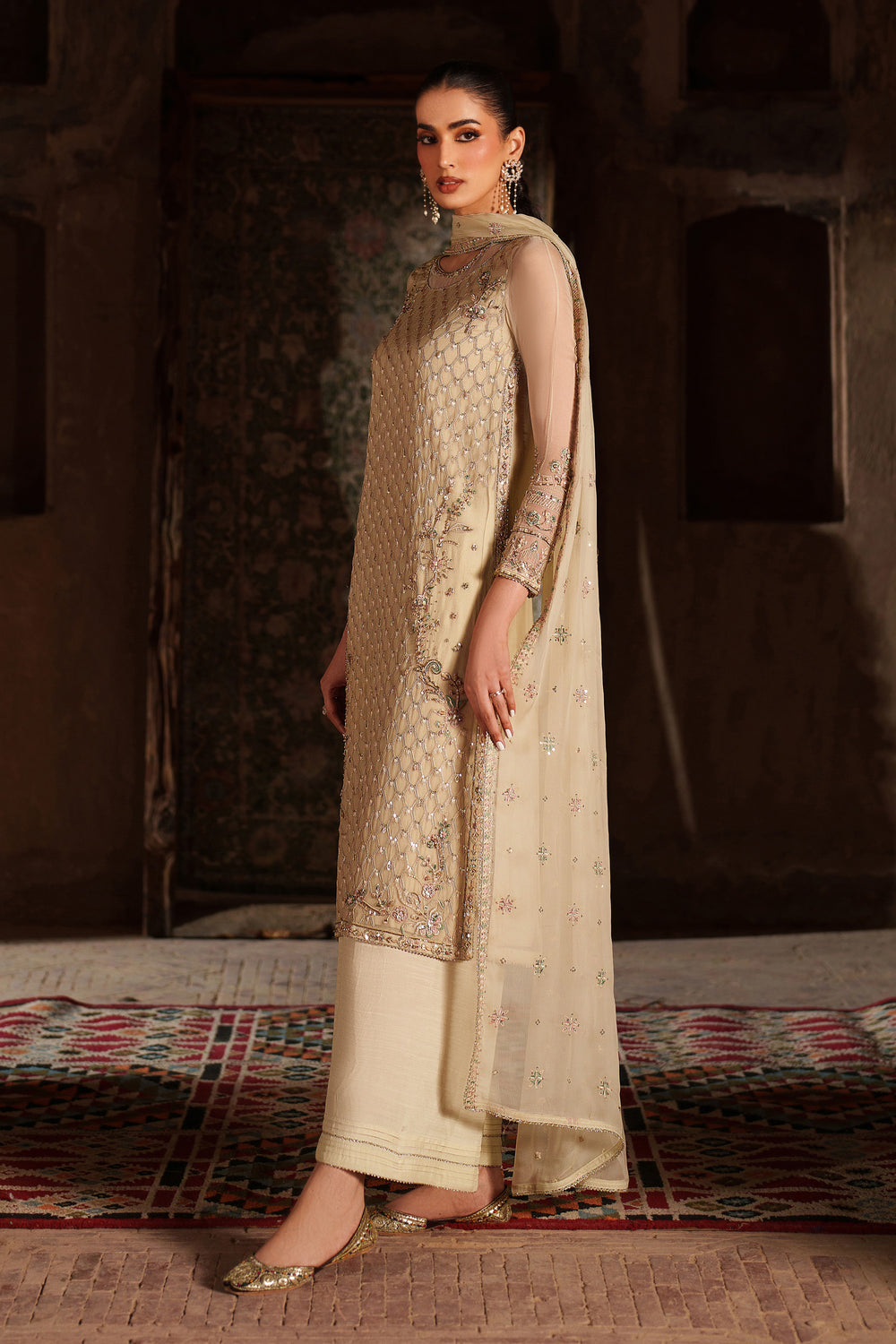 Woman in a traditional outfit with intricate patterns standing in a rustic setting.