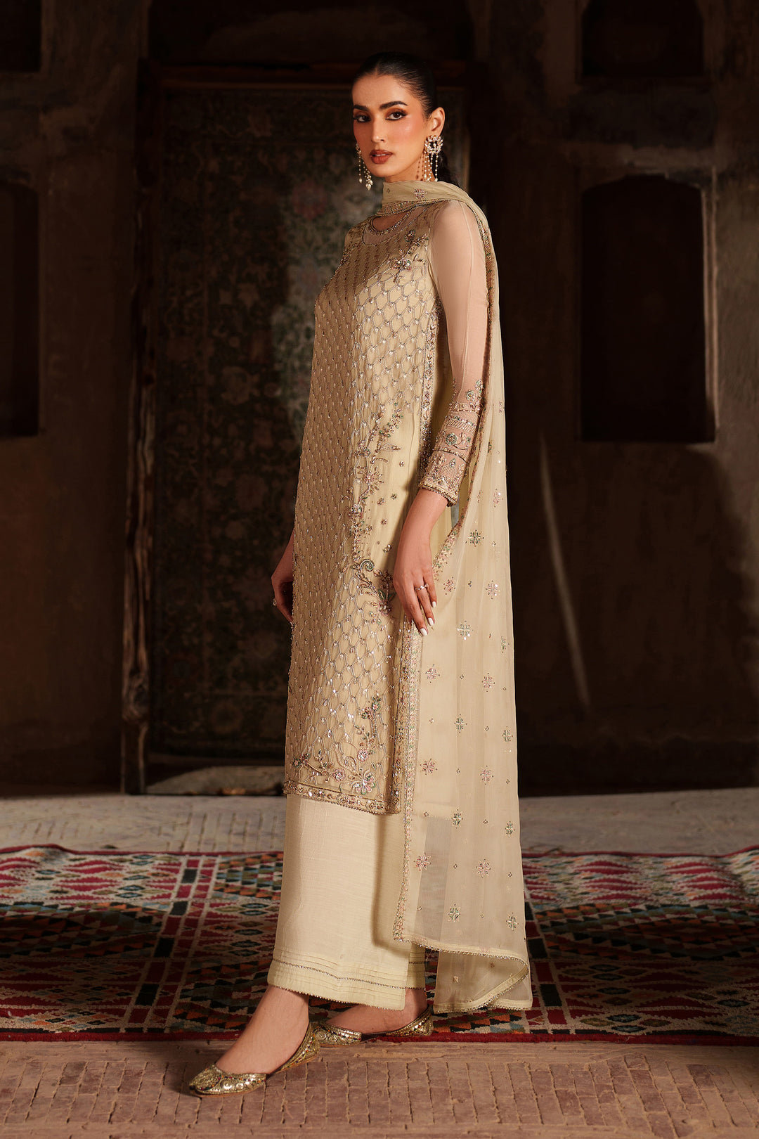 Woman in a traditional outfit with intricate patterns standing in a rustic setting.