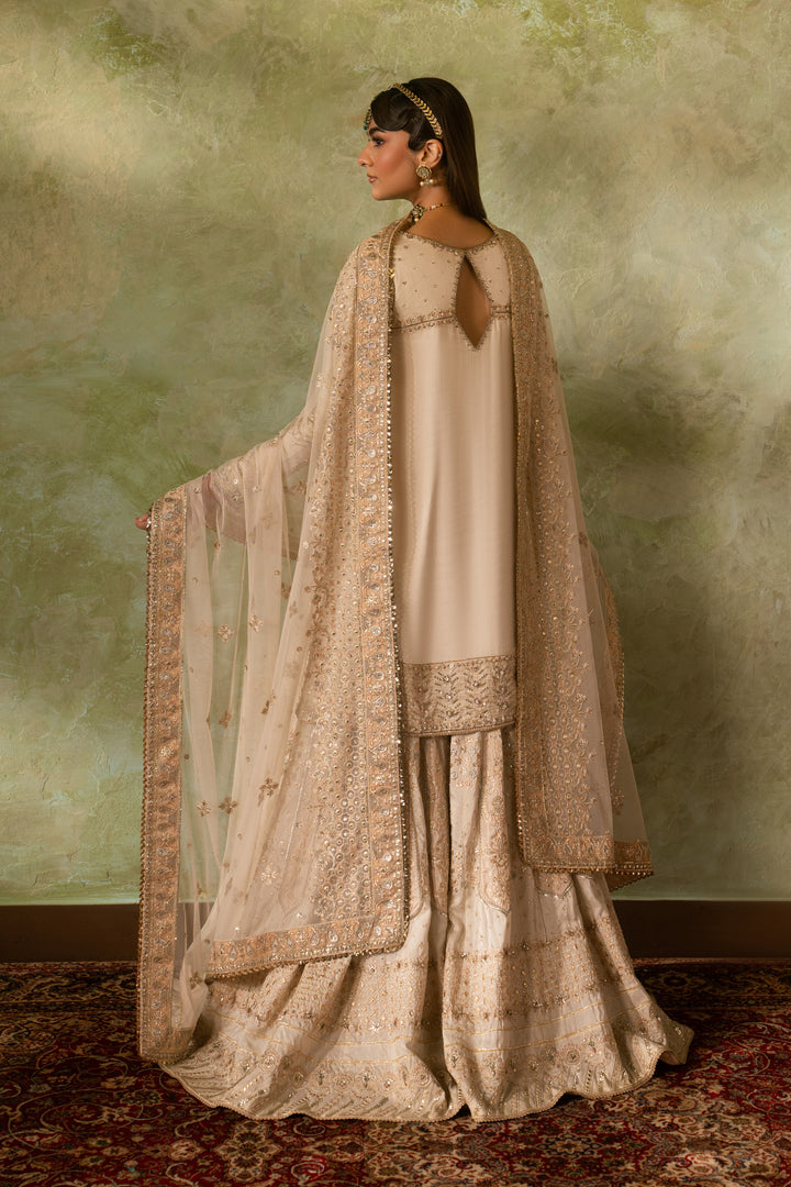 Back view of Damiya off white Nikkah dress showing smooth fall of silk shirt and wide sharara flare with light net dupatta, elegant ready made bridal formal outfit.