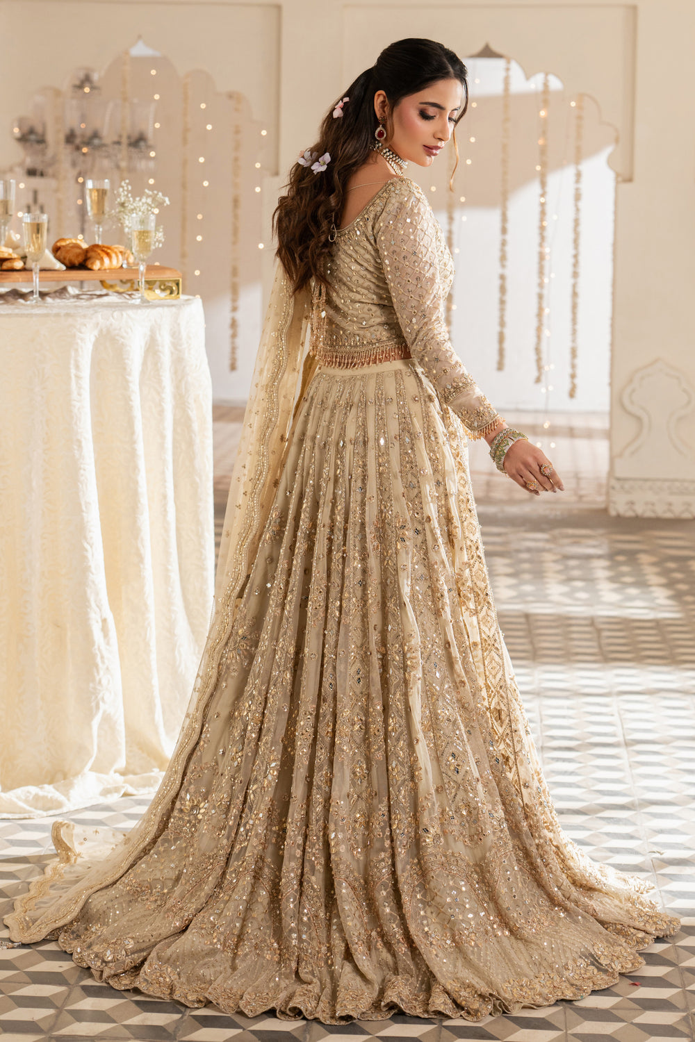Woman in a beige embroidered traditional outfit standing in a decorated room.
