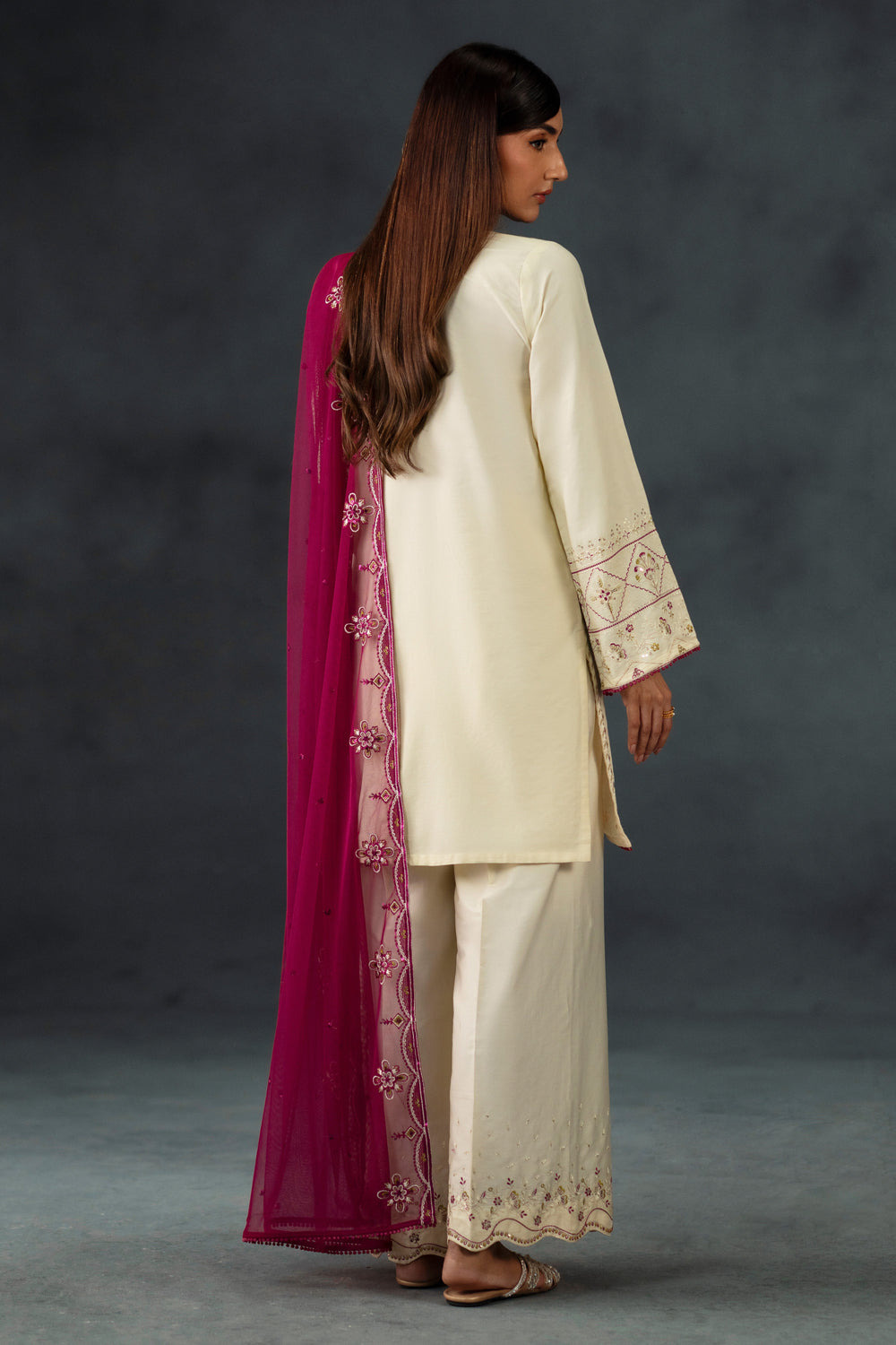 Woman in traditional cream outfit with pink dupatta against a dark background
