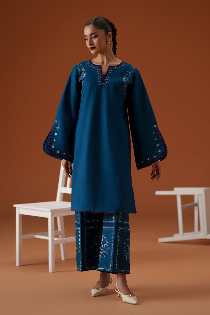 Model wearing Juni teal embroidered lawn outfit with printed chiffon dupatta and cambric culotte trouser for summer festive wear.
