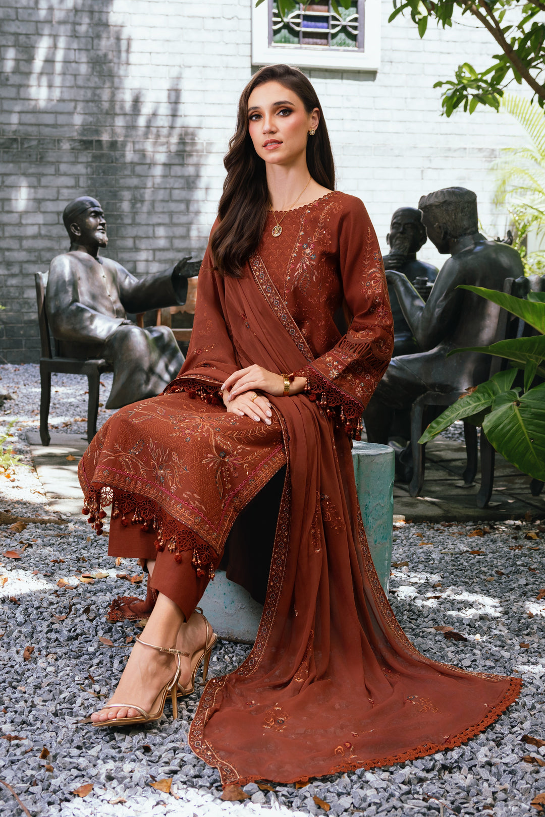 Seated pose of model wearing NAQSHI Farukh rust brown embroidered outfit highlighting fabric fall and elegant overall look