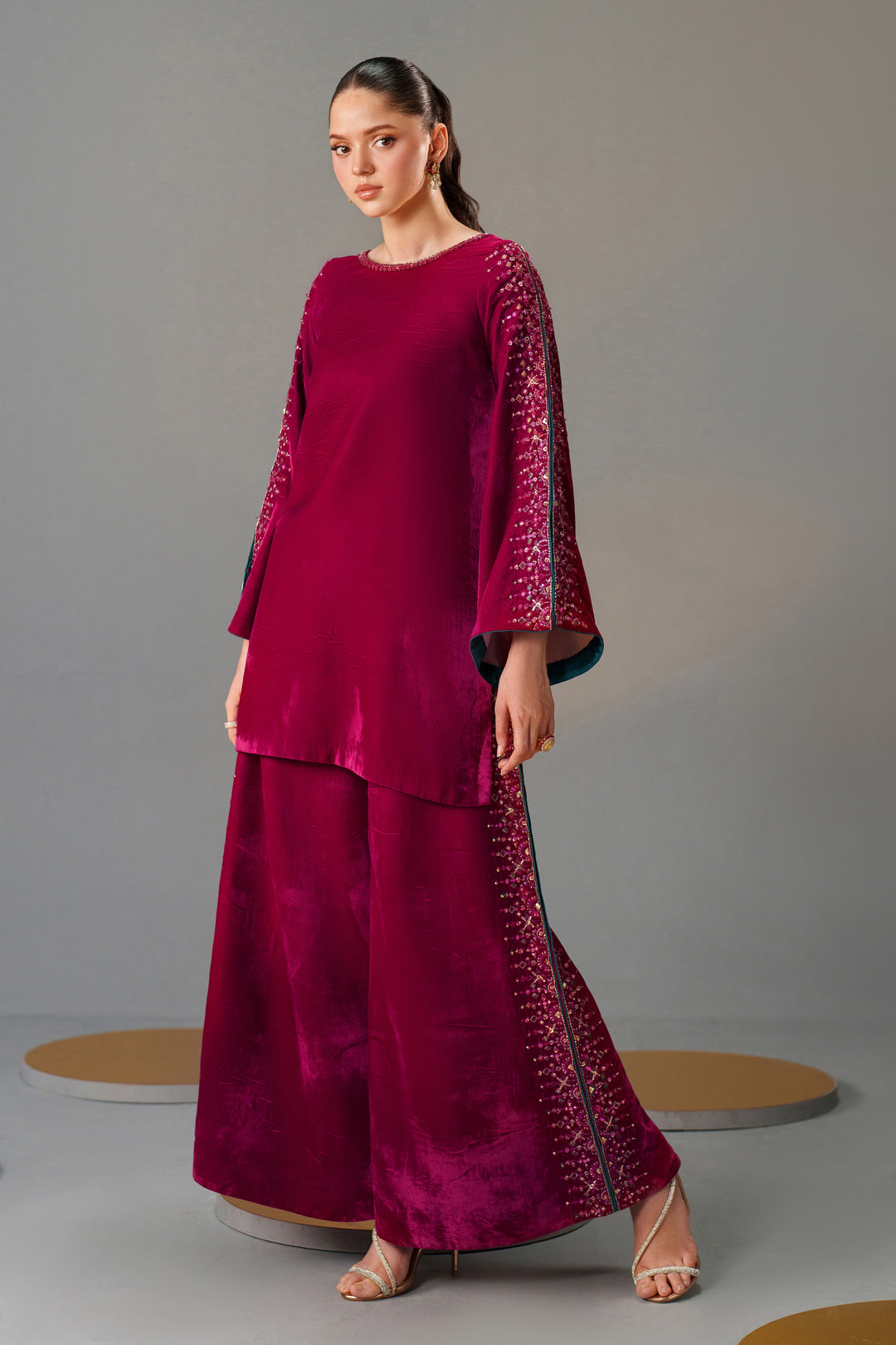 Woman wearing a magenta outfit with intricate patterns on a gray background
