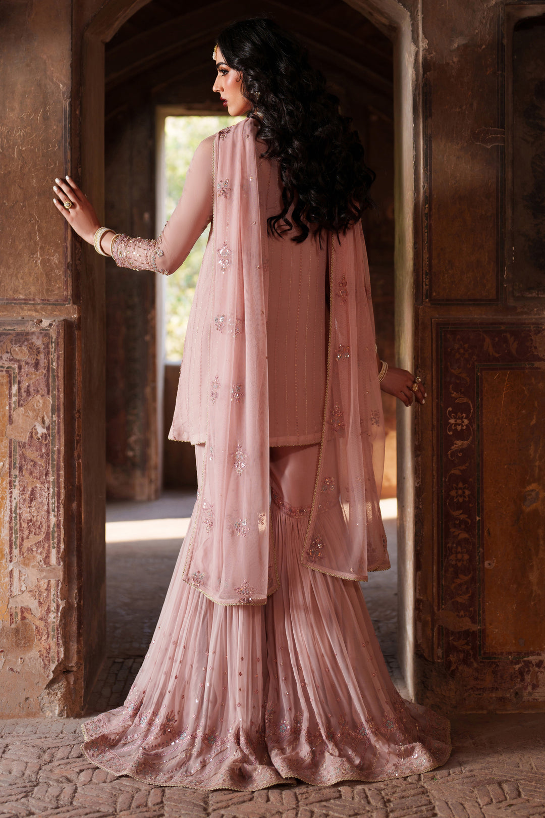 Woman in a traditional pink outfit standing in an ornate doorway.