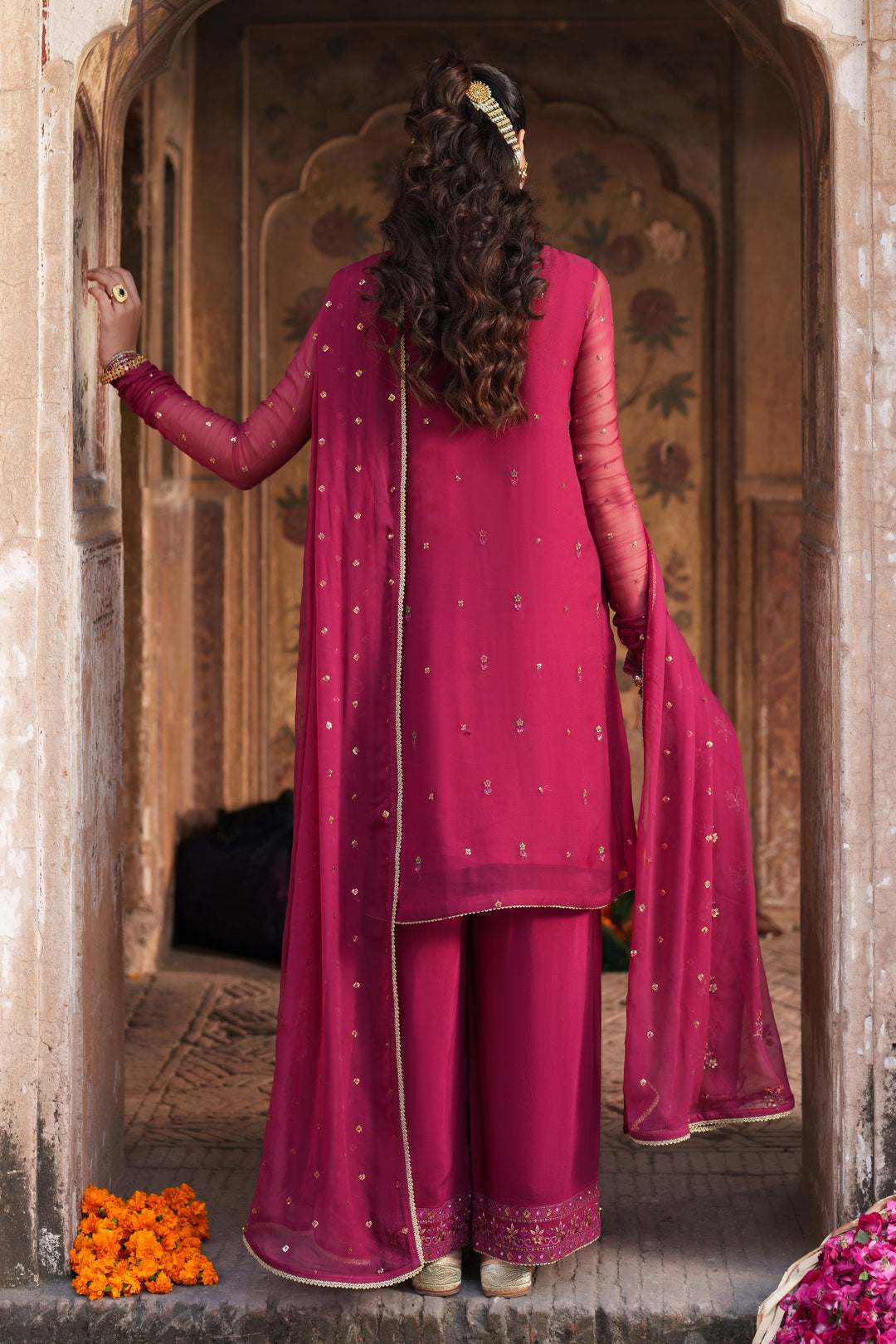 Person wearing a pink traditional outfit standing in an archway.