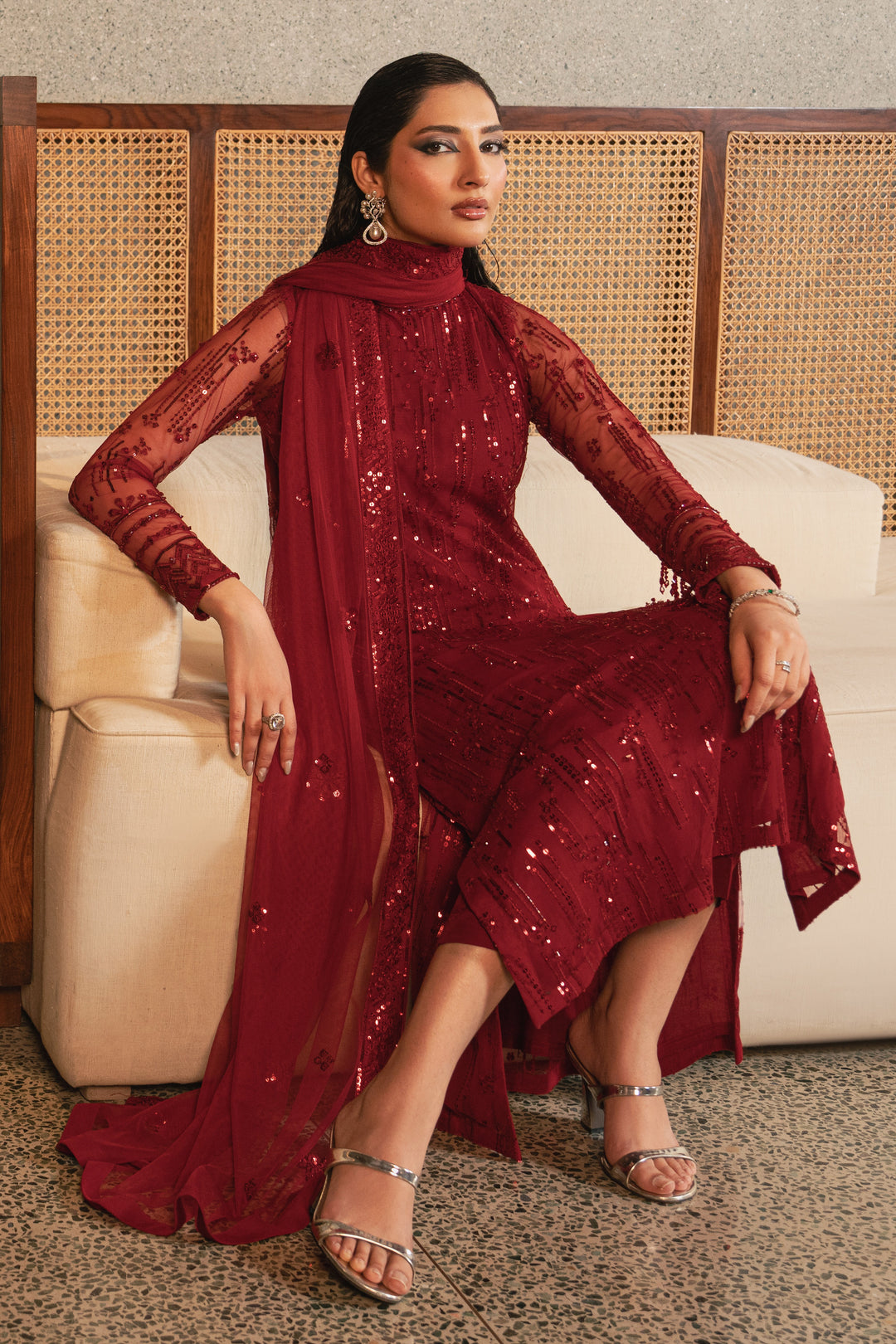 Seated view of NAQSHI Valentina rose red net 3-piece outfit highlighting straight cut trousers, flowing net dupatta, and elegant formal styling.