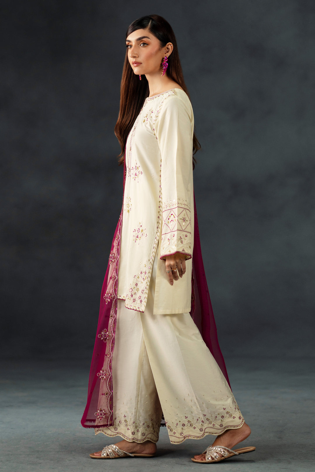 Woman wearing a cream embroidered outfit with a dark background
