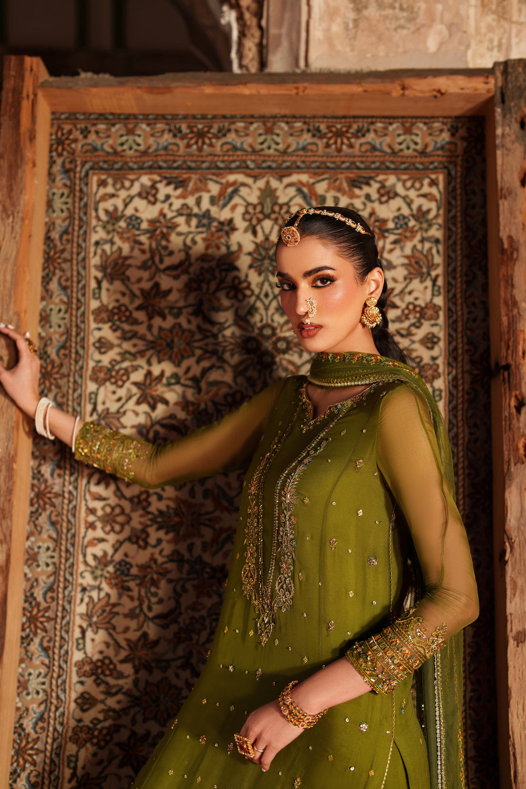 Woman in a green traditional outfit standing against an ornate wall.