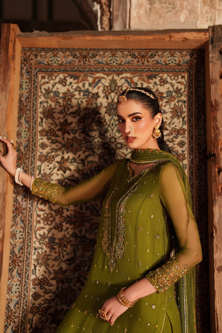 Woman in a green traditional outfit standing against an ornate wall.