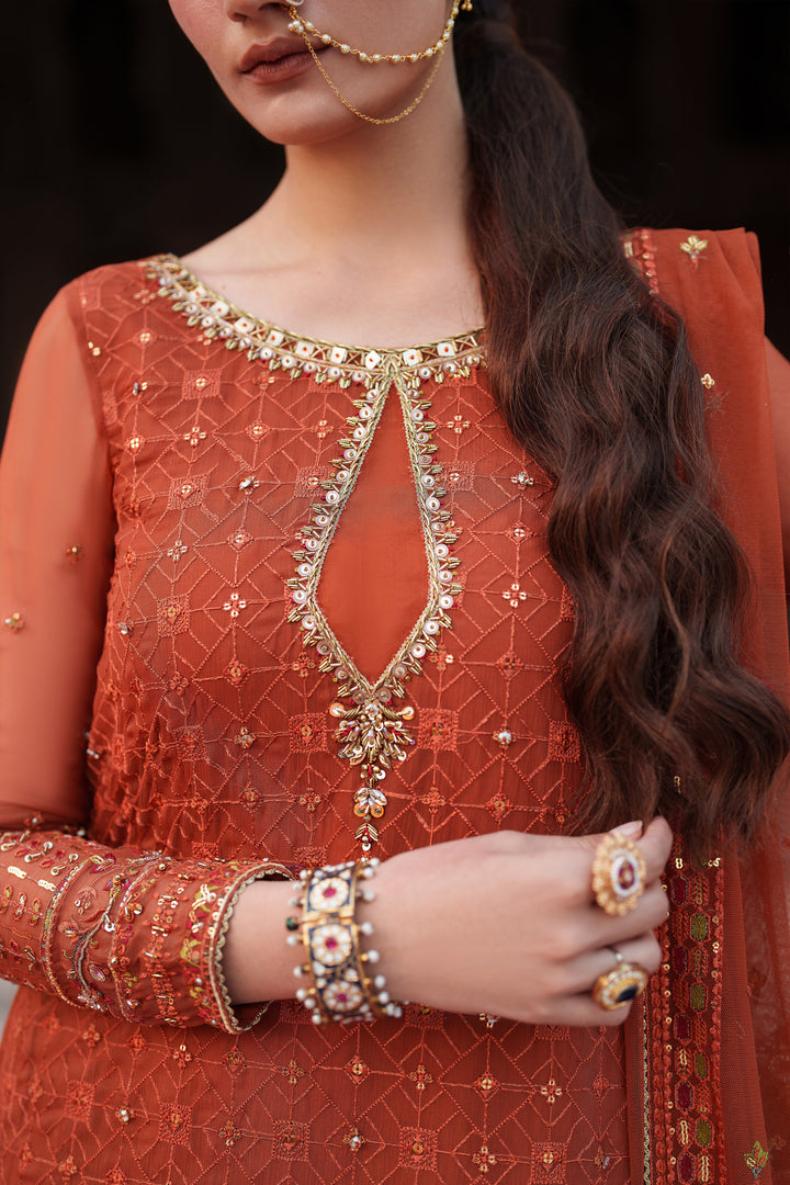 Woman wearing an orange embroidered traditional outfit with gold jewelry.