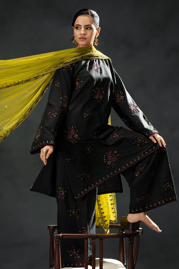 Woman in a black traditional outfit with yellow dupatta against a dark background
