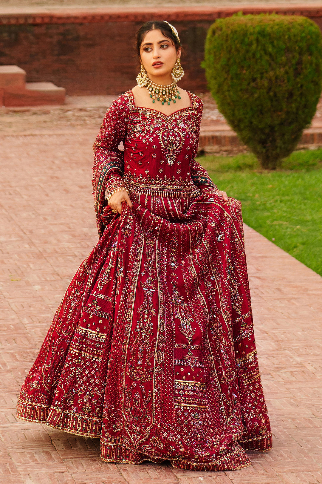 NAQSHI Gul Kand red bridal lehenga styled outdoors with full flare skirt and ornamental embroidery for wedding functions.