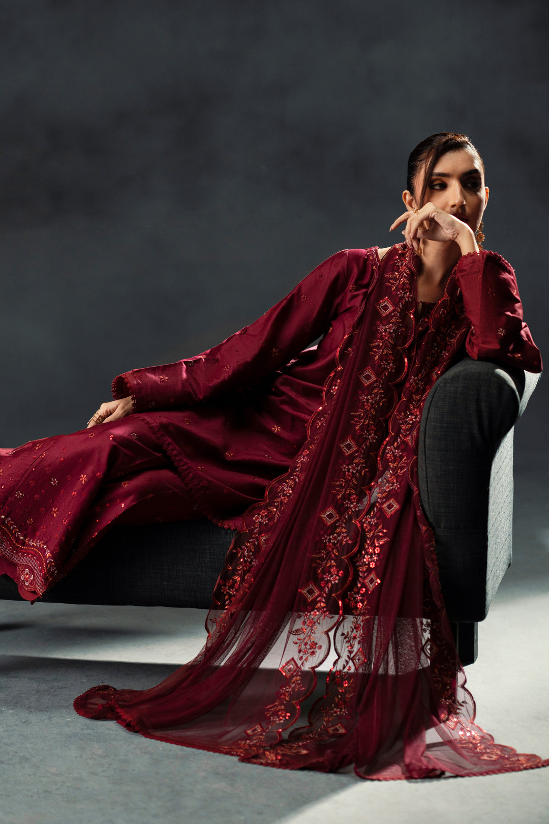 Person wearing a burgundy embroidered outfit against a dark background