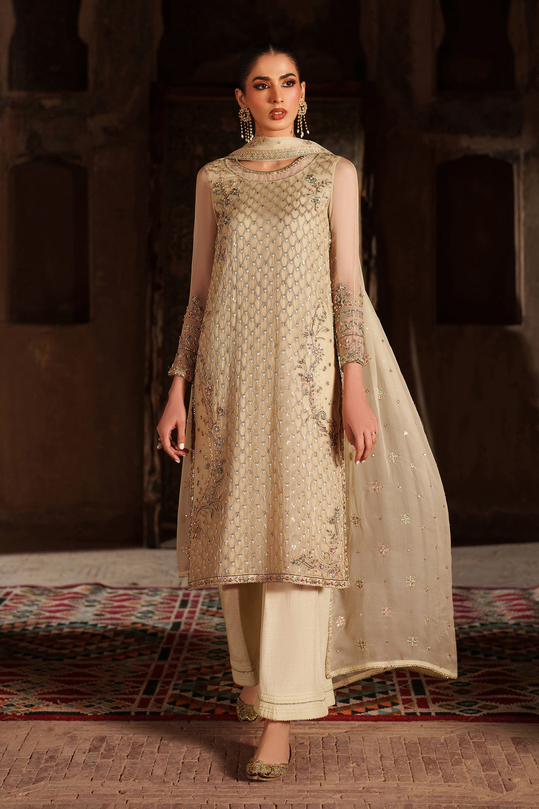Woman in a traditional outfit with intricate patterns on a textured floor.