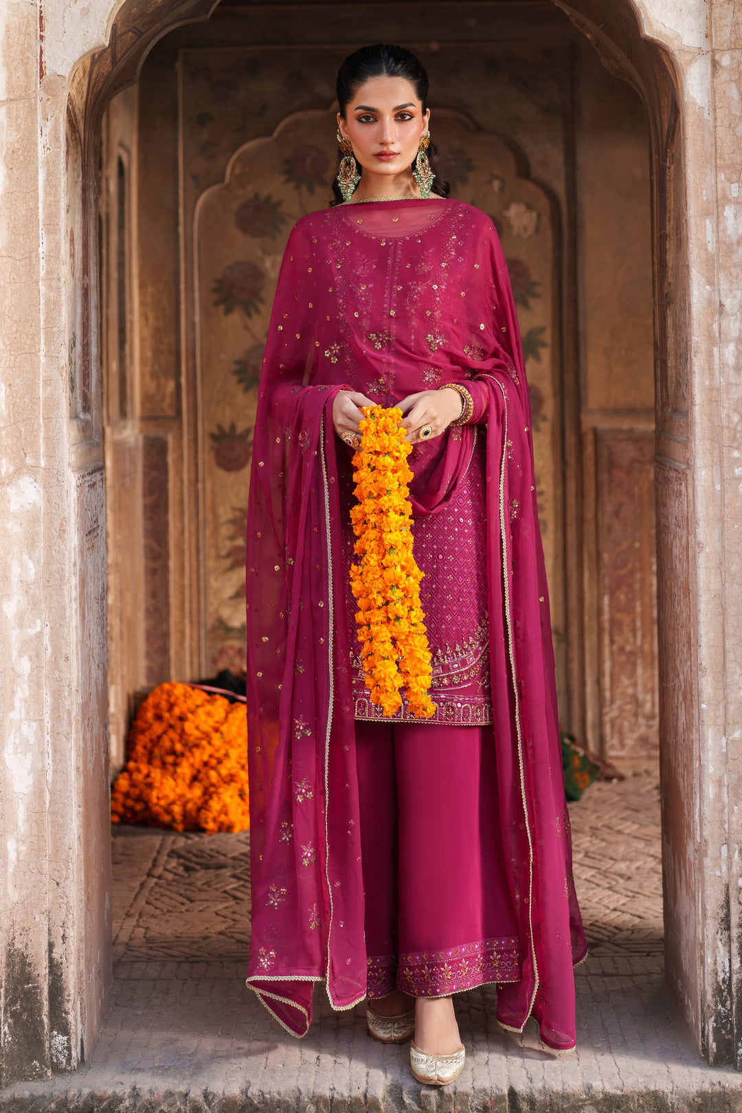 Woman in a traditional maroon outfit with yellow flowers standing in an archway.