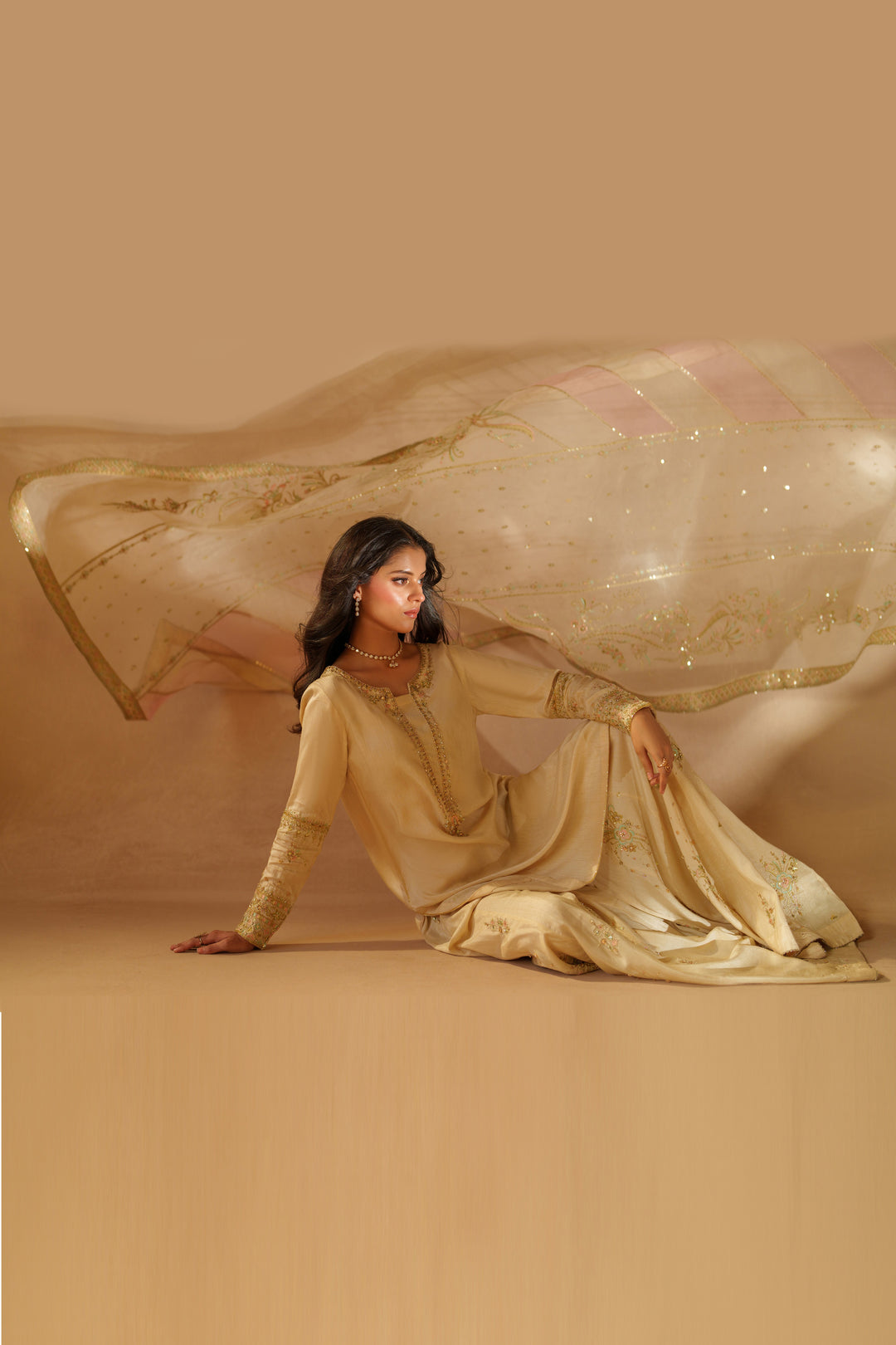 Styled artistic shot of NAQSHI Mawrah beige sharara outfit with sheer organza dupatta spread, showcasing premium finishing and event-ready elegance