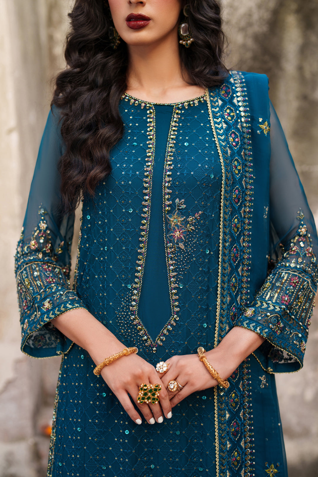Woman wearing a teal embroidered traditional outfit with jewelry.