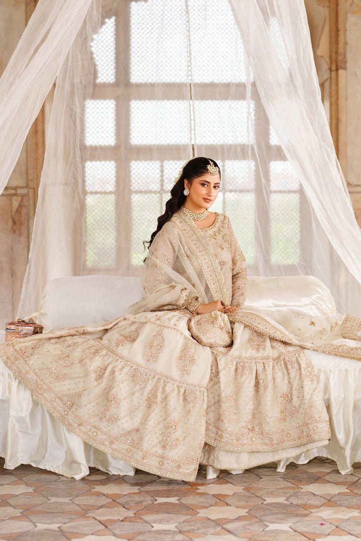 Sitting pose of NAQSHI Aneeqa ivory beige bridal-style dress with detailed embellishment and full skirt for formal celebration looks.