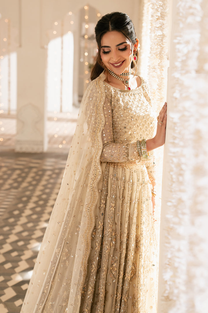 Woman in a traditional outfit with a gold and white theme, standing indoors.