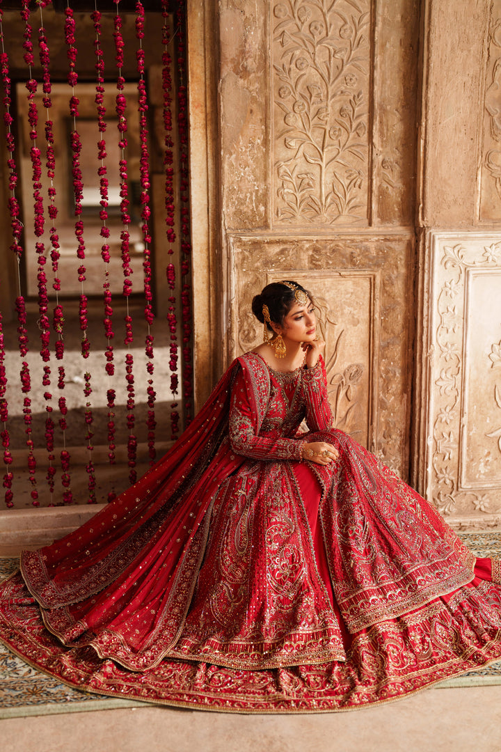 Woman in a red traditional outfit sitting in an ornate room.
