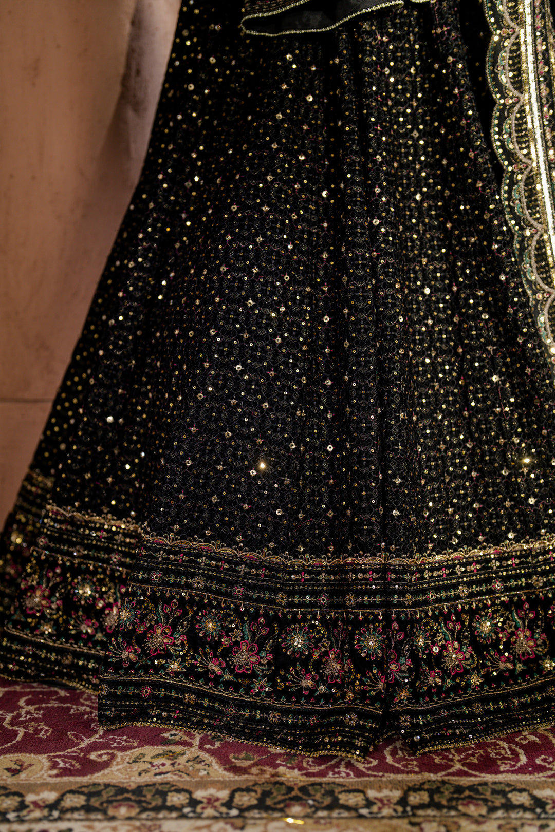 Close-up of a black embroidered garment with gold details on a patterned surface.