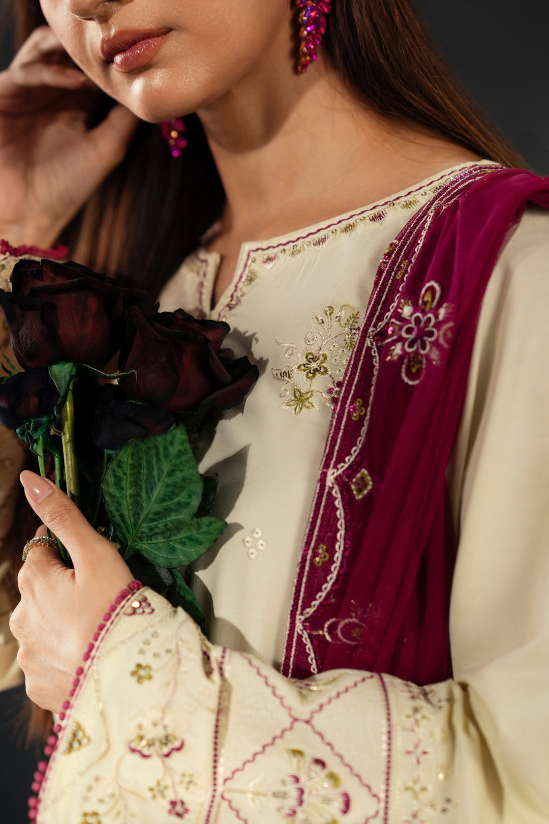 Woman wearing a traditional embroidered outfit with a purple shawl, holding dark flowers.
