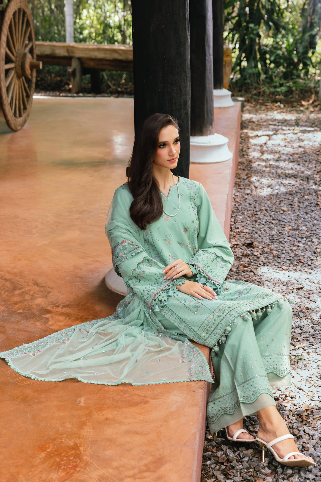 Woman in a light green traditional outfit sitting on a wooden bench outdoors.
