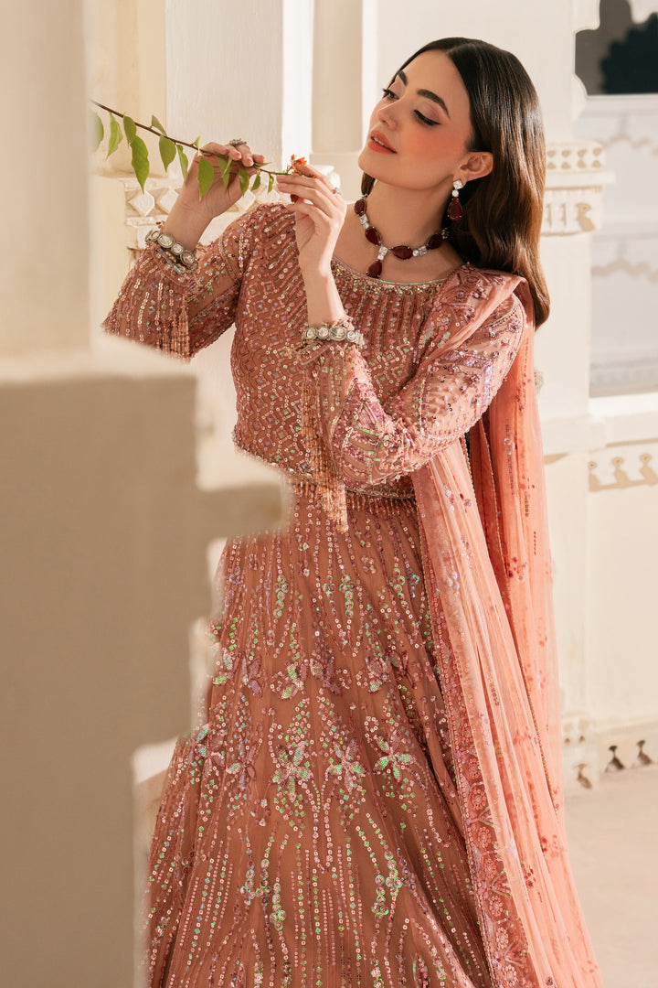 Woman in a detailed pink traditional outfit holding a branch against a light background.