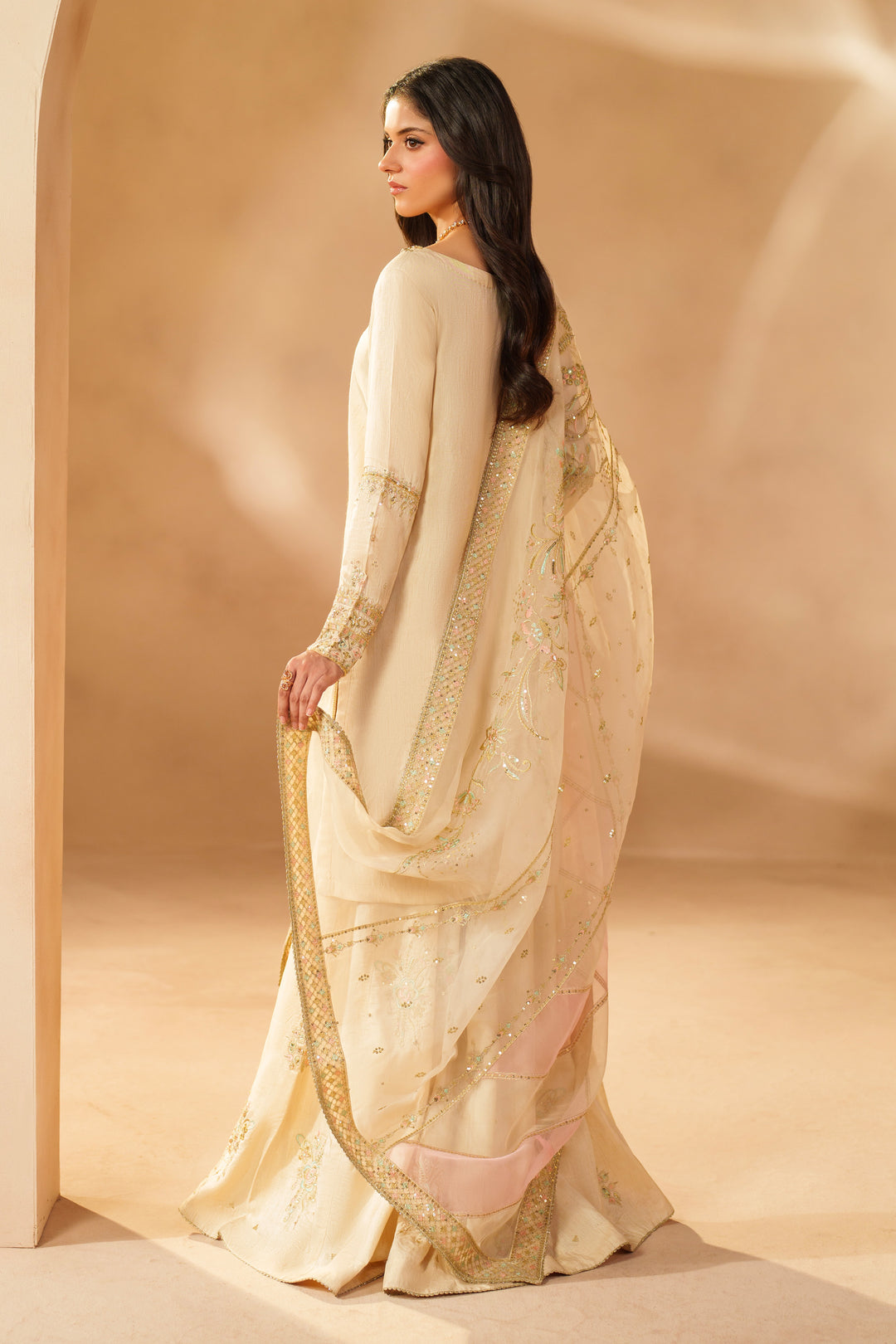 Side view of NAQSHI Mawrah beige formal sharara set showing the embroidered raw silk shirt, flowing sharara panels, and sheer organza dupatta styled for special occasions