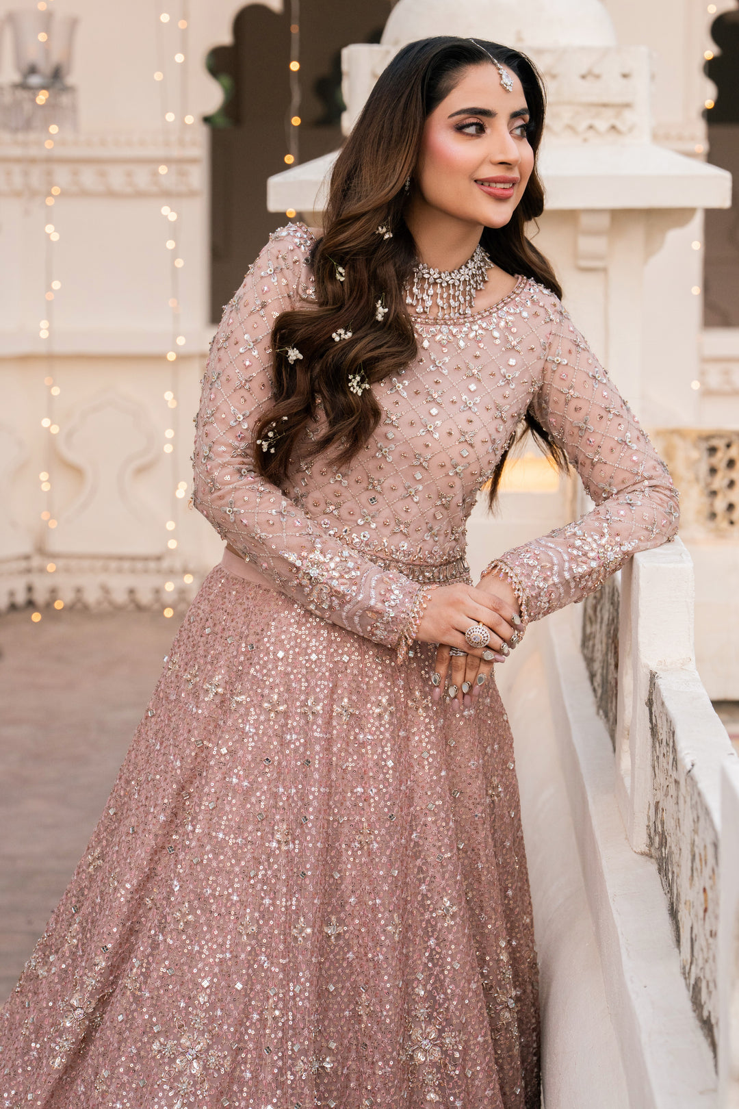 Woman in a sparkling pink dress standing in front of a decorative white structure.