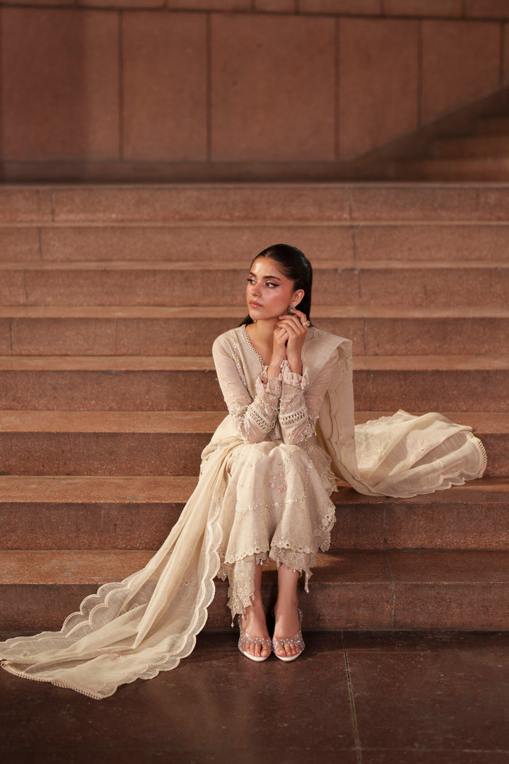 Seated pose of NAQSHI Ingrid off-white embroidered outfit with flowing khadi net shirt, PK raw silk trousers and cotton organza dupatta