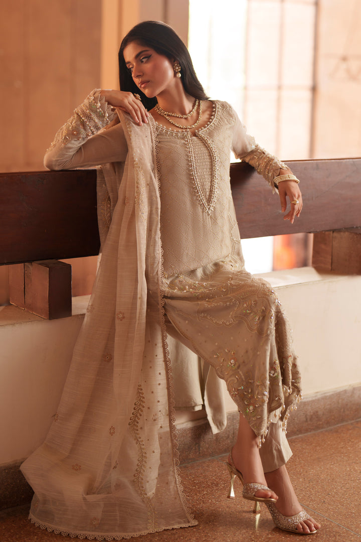Seated styling shot of NAQSHI Minera dusty beige formal outfit with embroidered khadi net shirt, raw silk trousers and cotton organza dupatta