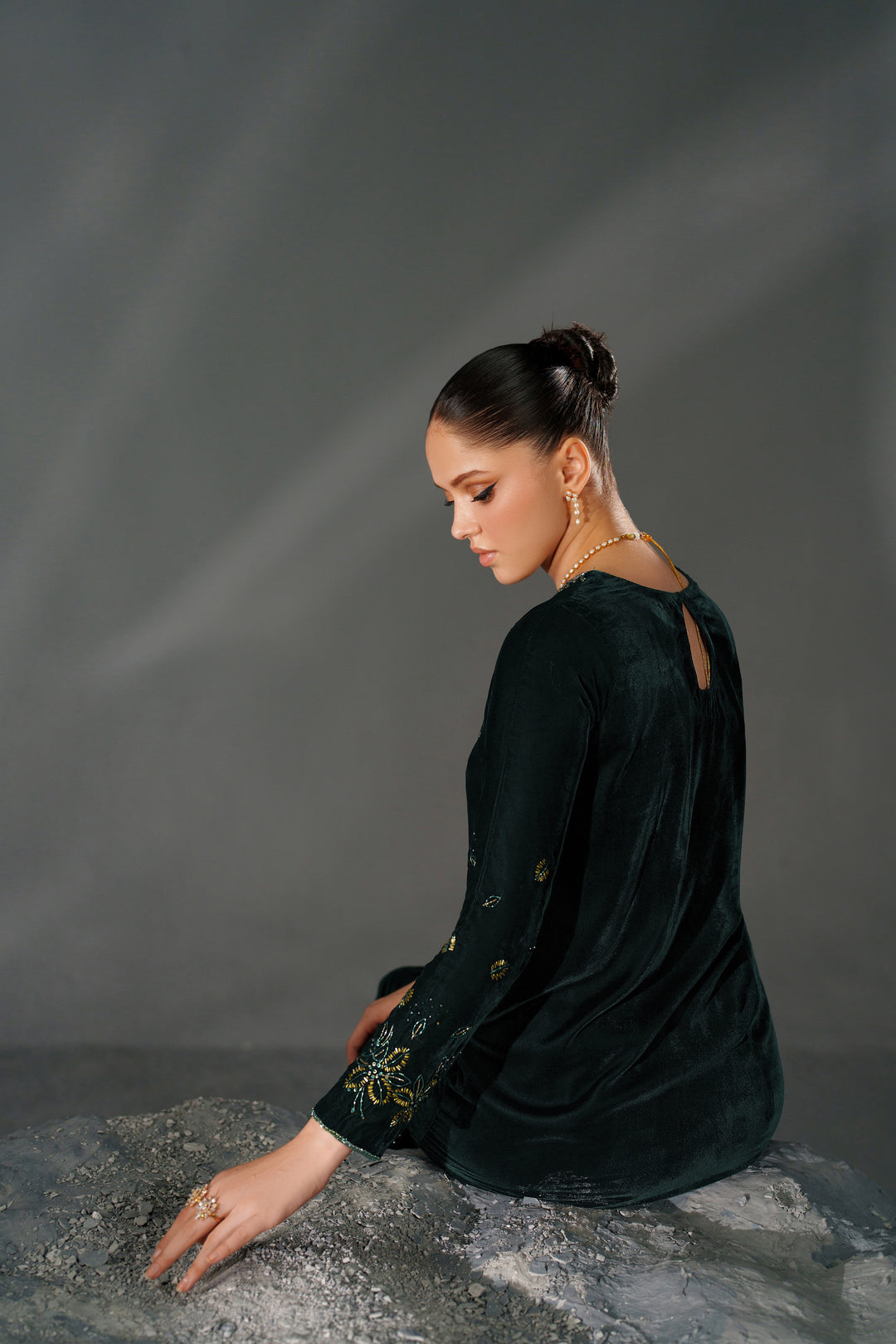 Woman in a dark green dress sitting on a textured surface with a gray background
